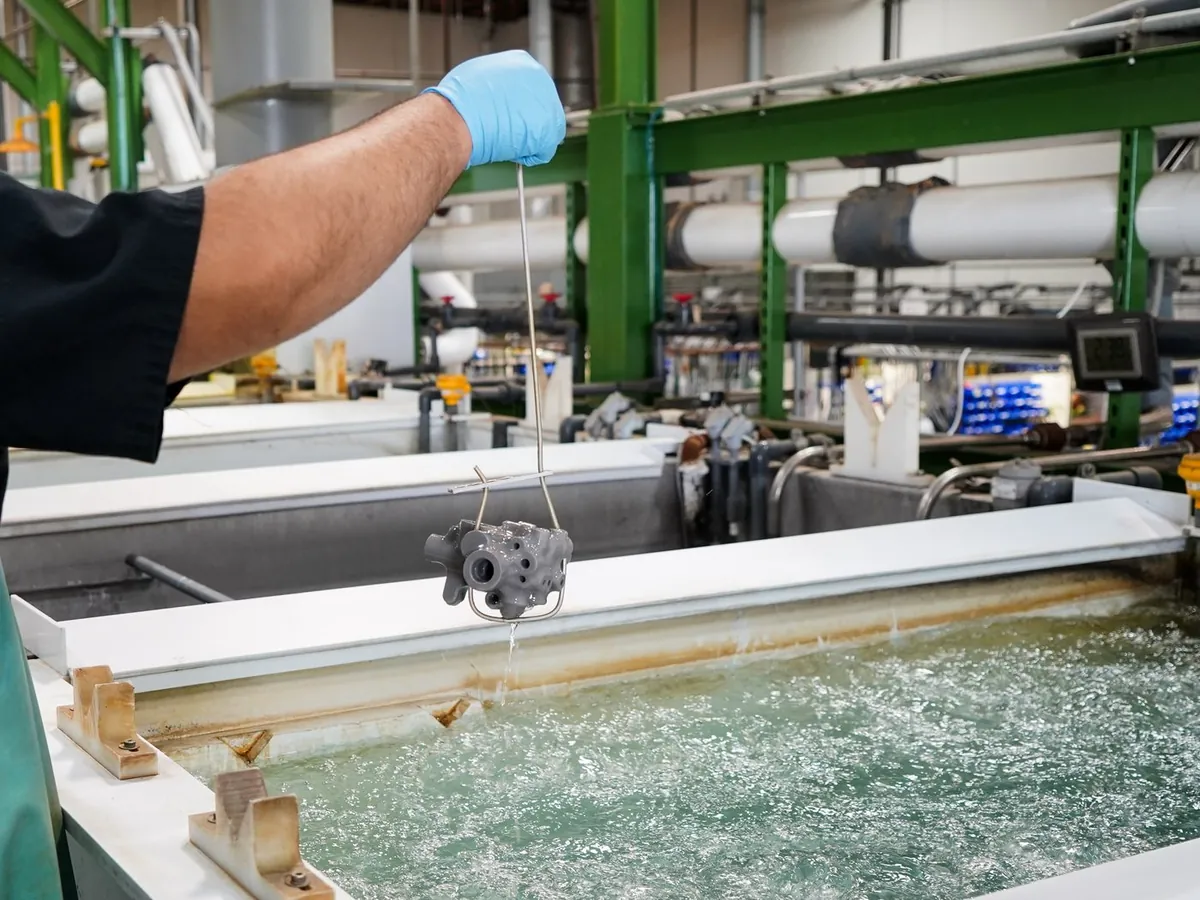 Technician lifting a part from a processing tank on the chemical processing line